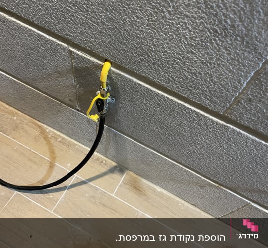 שסתום גז עם צינור שחור על קיר אפור